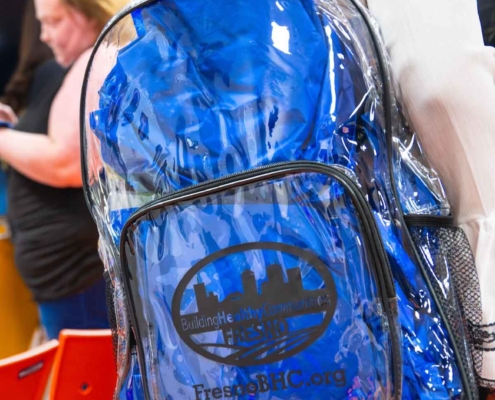 Close-up of a transparent blue backpack branded with the Building Healthy Communities Fresno logo, highlighting the supportive resources and tools provided through the Fresno BHC Youth Internships Program for aspiring youth leaders.