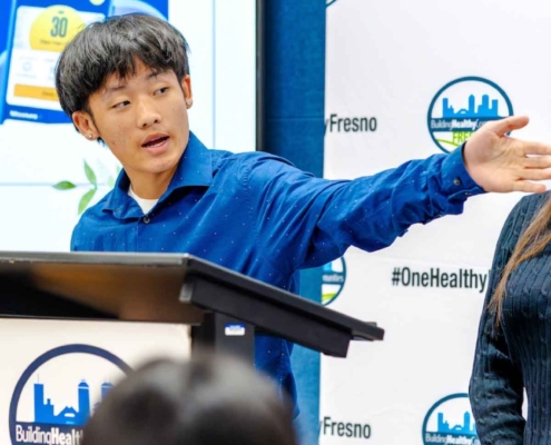 A determined youth intern in a blue shirt leading a presentation at the Fresno BHC event, exemplifying the program’s focus on youth empowerment and urging peers to apply.