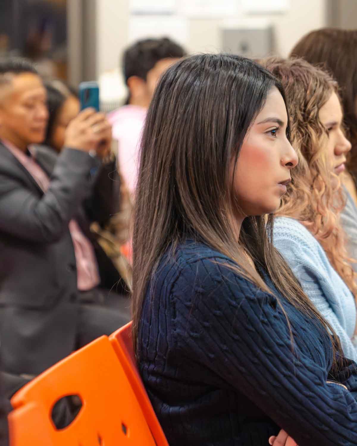 A young woman in a navy sweater attentively listening during the Fresno BHC Youth Internships Program session, reflecting focused engagement and commitment to community leadership.