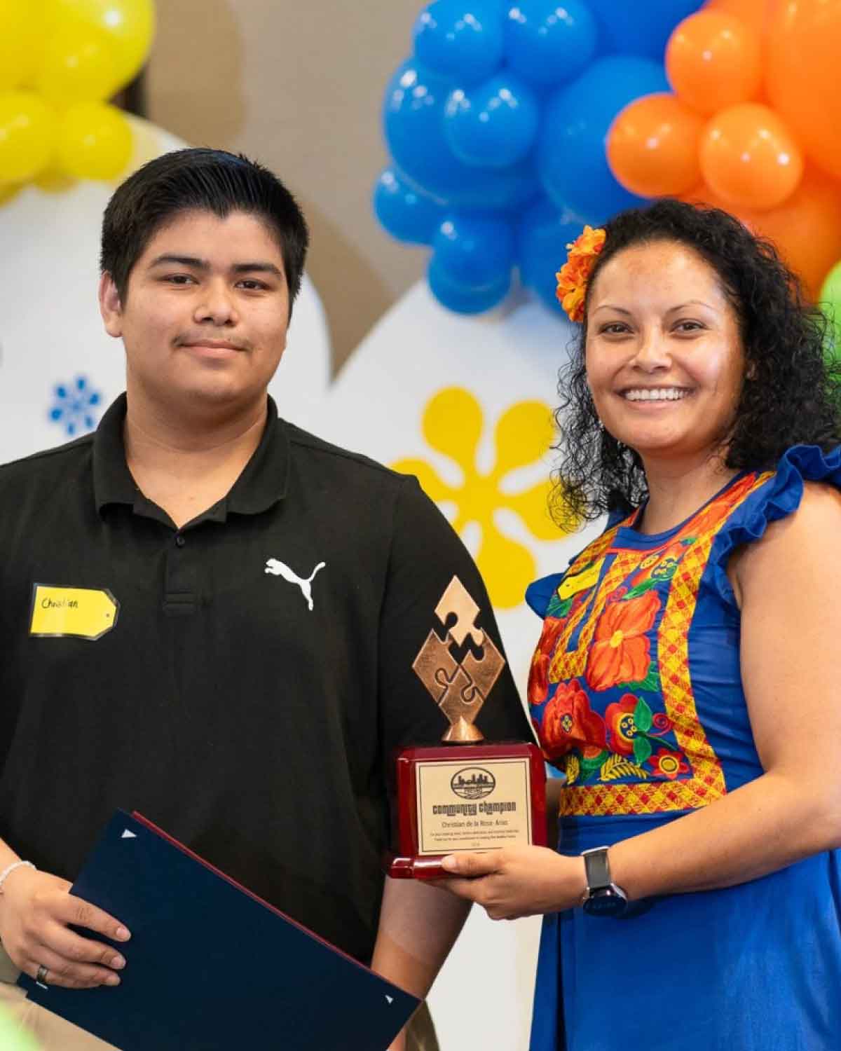 A young participant receiving a ‘Conquest Champion’ award alongside a Fresno BHC mentor in vibrant traditional attire, celebrating youth accomplishments and encouraging peers to join the leadership program.