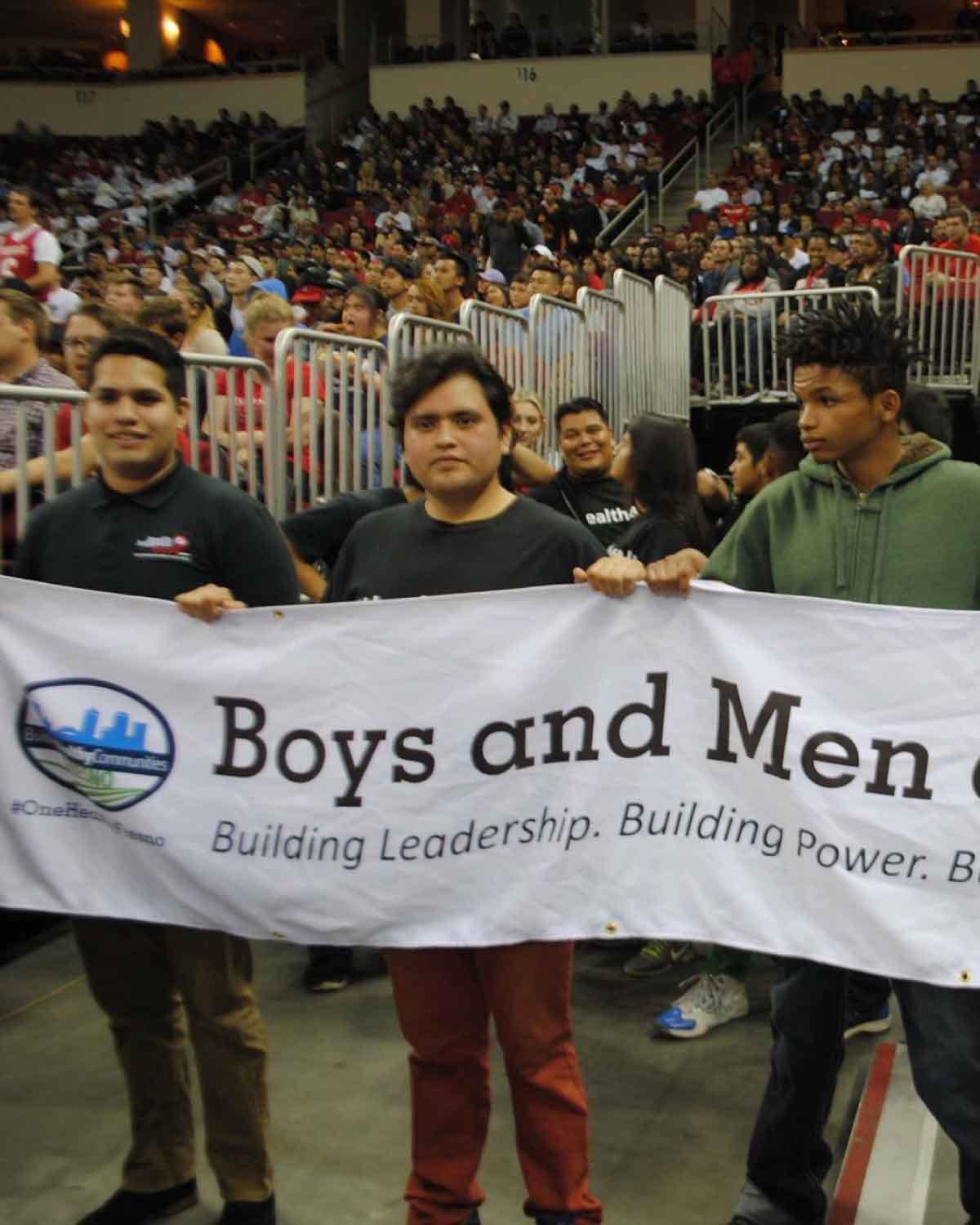 Boys and Men of Color participants standing in an arena and holding a banner that reads ‘Building Leadership. Building Power. Building Community,’ exemplifying Fresno BHC’s dedication to empowering youth and encouraging them to join the Youth Internships Program.