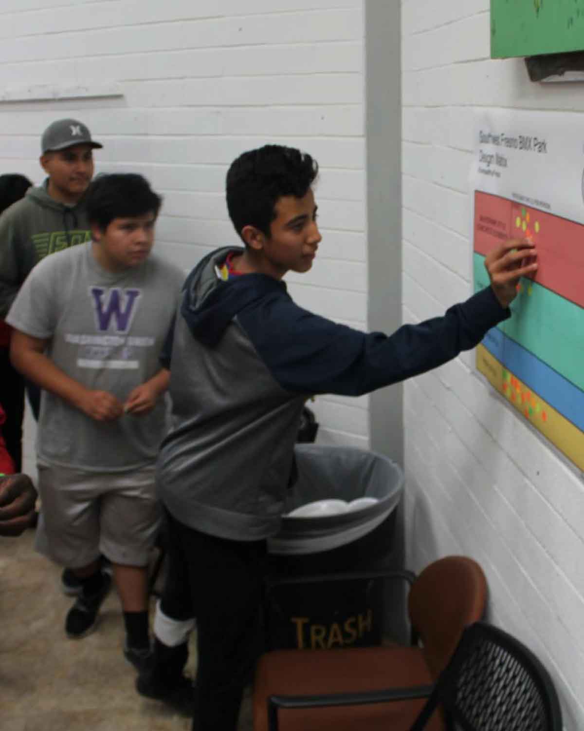 A youth participant placing stickers on a color-coded chart during a Fresno BHC workshop, showcasing active community engagement and hands-on learning opportunities for aspiring youth leaders to apply for the program.