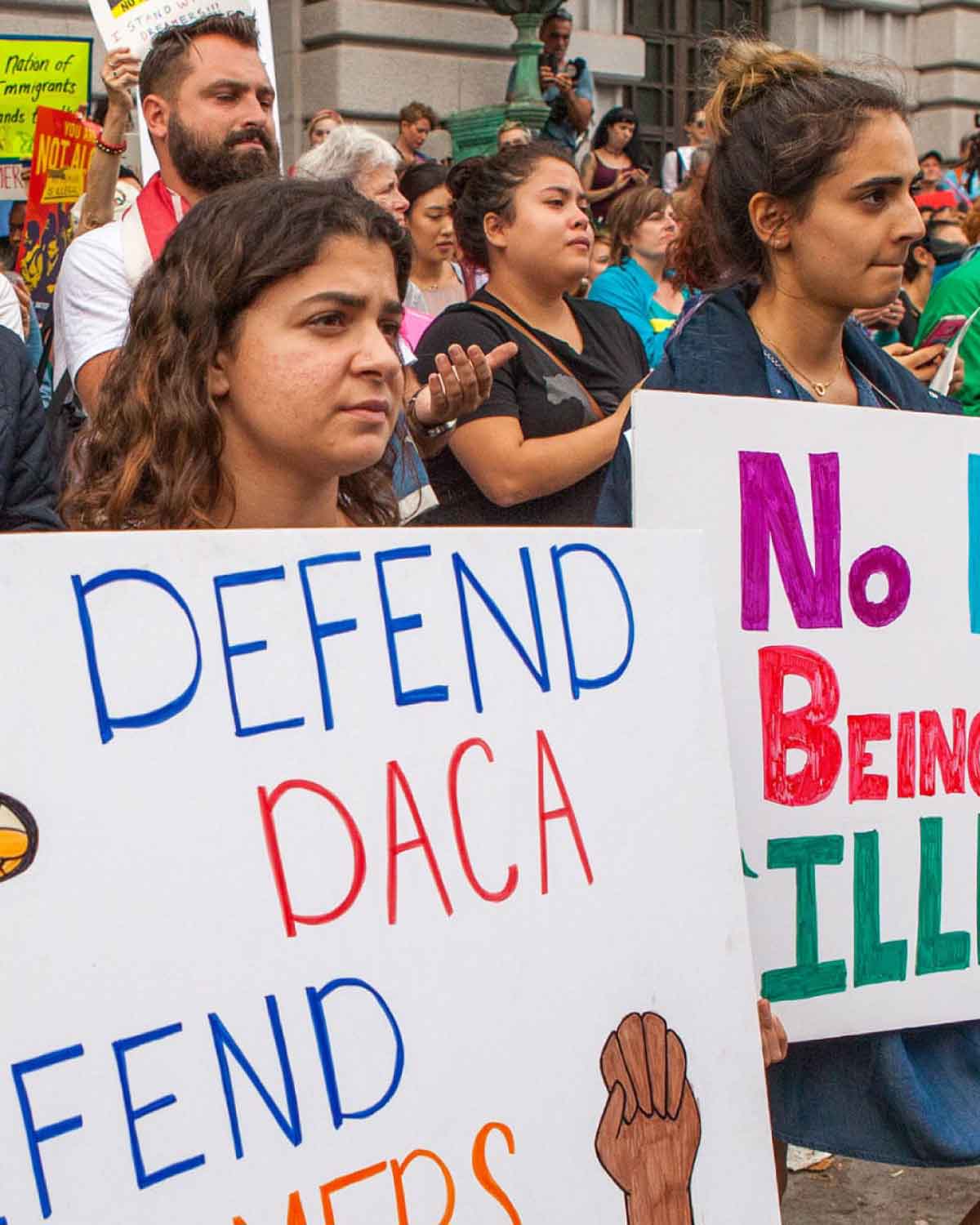 A group of demonstrators gathered at a rally, holding signs with messages such as ‘Defend DACA, Defend Dreamers’ and ‘No human being is illegal.’