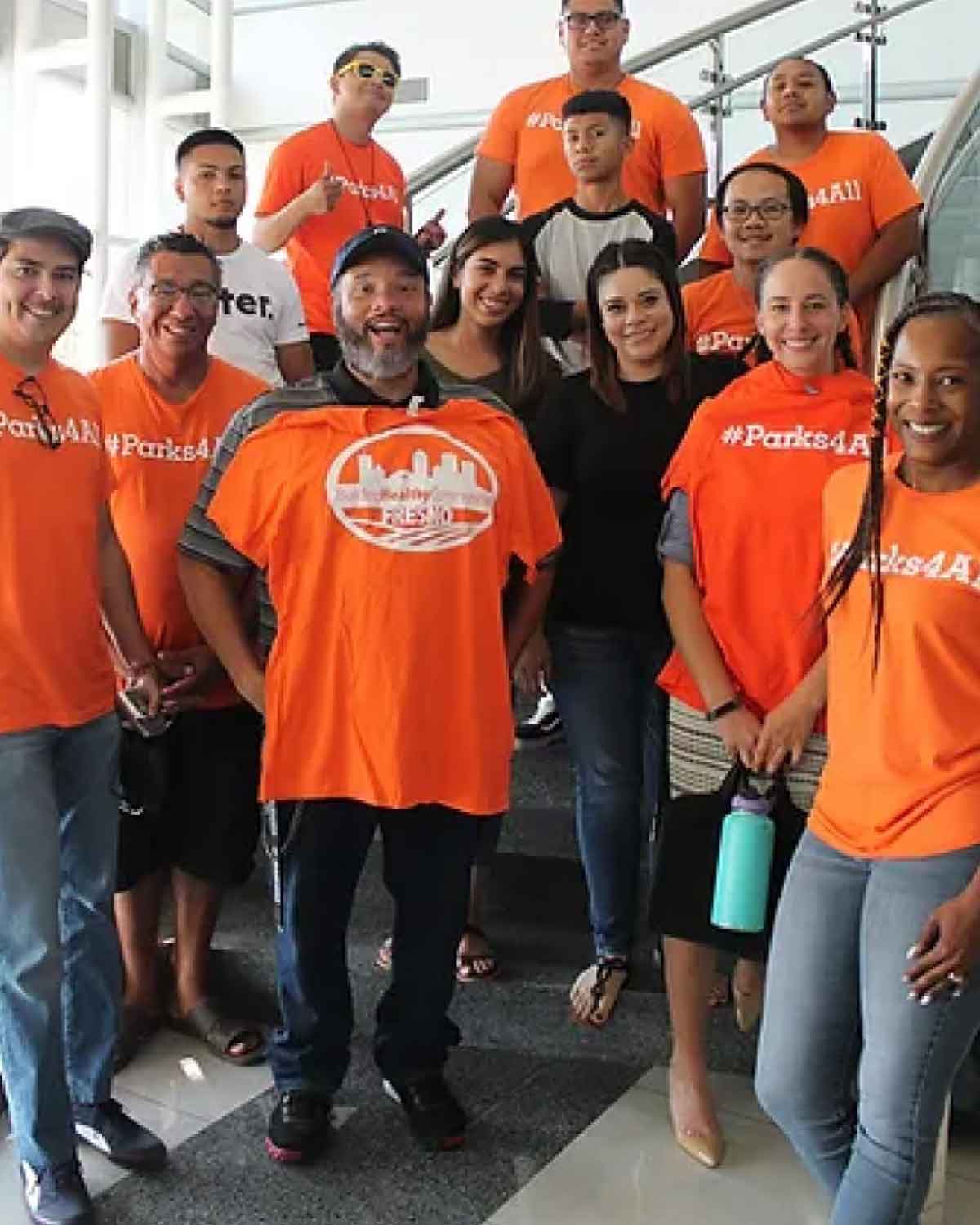 A group of people wearing orange ‘#Parks4All’ T-shirts gathered on a stairway, smiling and posing together.