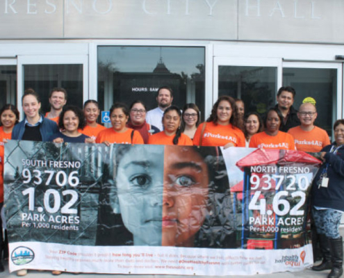 Advocates stand in front of Fresno City Hall holding a banner highlighting disparities in park access between South and North Fresno neighborhoods.