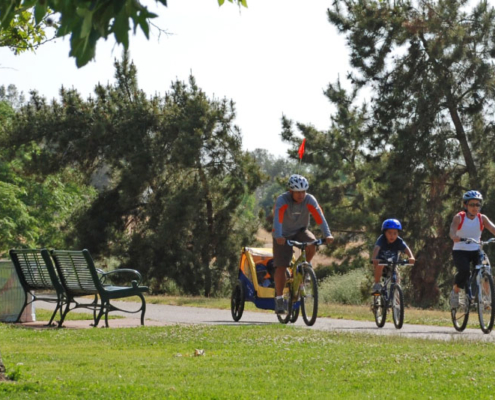 A family enjoys cycling along a scenic bike path in Fresno, showcasing the benefits of well-maintained parks and recreational spaces.