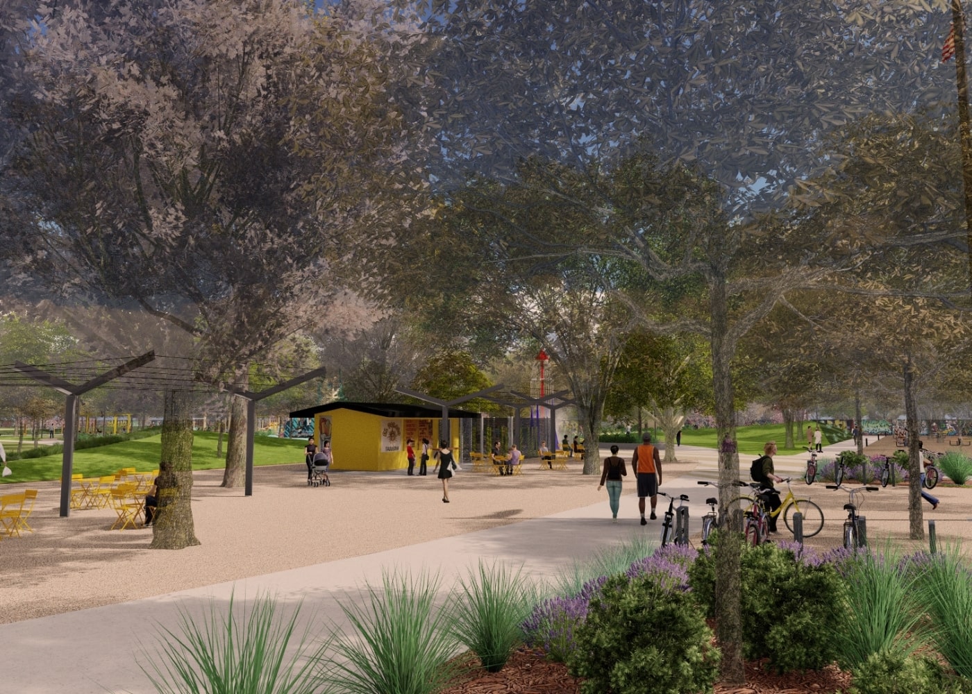 People walk and cycle through a shaded park pathway near the food stand and misting rocket structure, surrounded by lush landscaping.