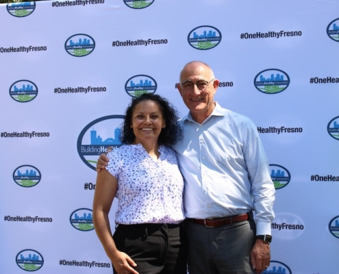 Two community leaders smile in front of the One Healthy Fresno backdrop at the Calwa Park groundbreaking event.