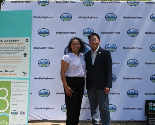 Calwa Park leader stands with state official in front of the bilingual “Our Park. Our Legacy.” sign during the groundbreaking ceremony.