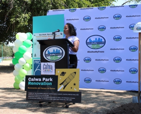 Keynote speaker delivers remarks at the podium during the Calwa Park Renovation launch, with balloons and project signage behind.
