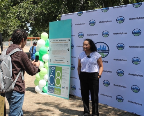 Community member films Calwa Park leader during a media interview at the groundbreaking celebration.