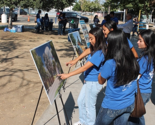 Youth attendees in blue shirts excitedly examine design boards showcasing future park amenities at the Calwa Park groundbreaking.