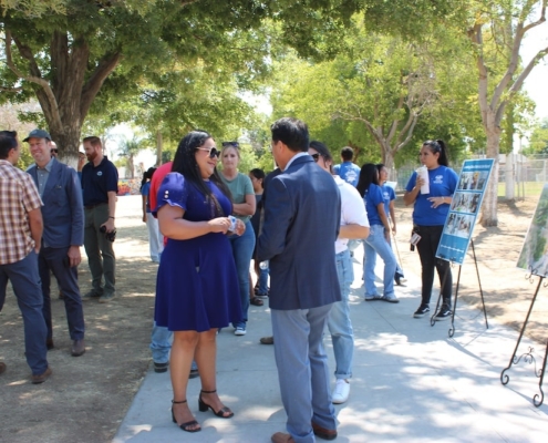 Community members, organizers, and residents engage in conversation during the Calwa Park Renovation event surrounded by project visuals and outreach tables.