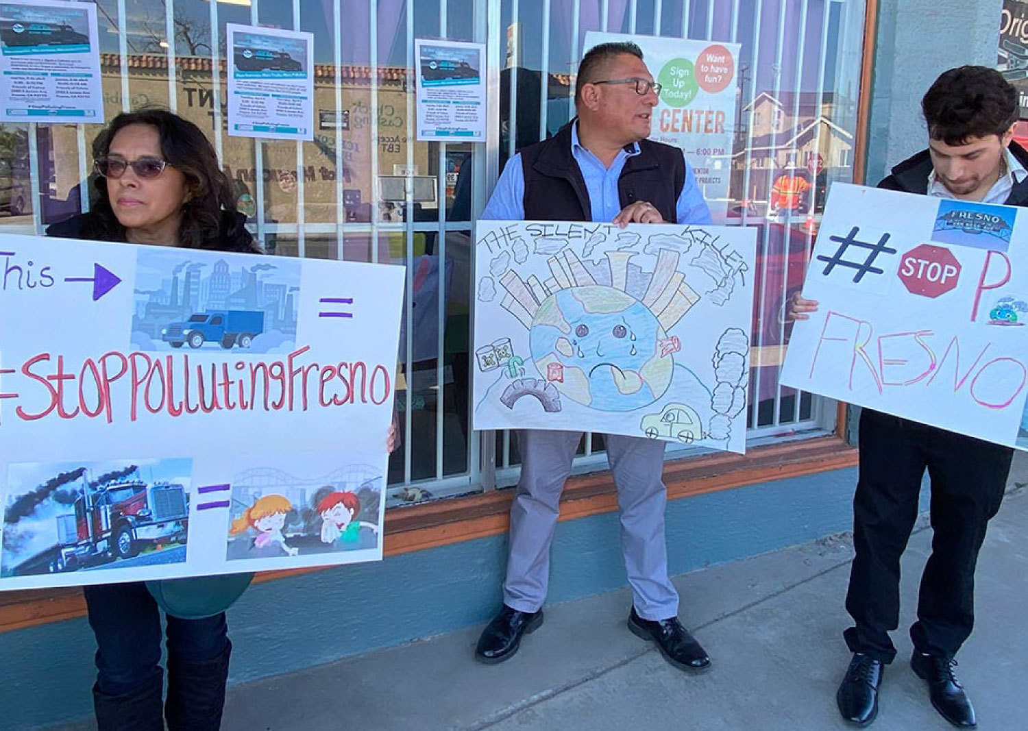 Community members in Fresno holding signs against freeway expansion and diesel truck pollution” 
/>
<img src=