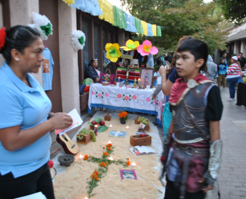 Día de los Muertos-inspired altar with candles, flowers, and food offerings at the Well-O-Ween community fair