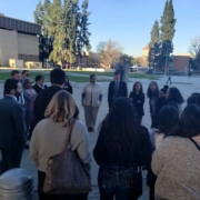 Did Caltrans Shortchange South Fresno? Judge Weighs Highway 99 Expansion Lawsuit A view from the opposite side of the circle, looking toward a different set of buildings and tall pine trees. The group is engaged in a discussion, with shadows stretching across the pavement in the afternoon light.