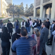 Did Caltrans Shortchange South Fresno? Judge Weighs Highway 99 Expansion Lawsuit A shot from behind the group, focusing on the speaker and the attentive audience. A man in a blue puffer jacket is in the foreground, and several people in professional suits are scattered throughout the circle.