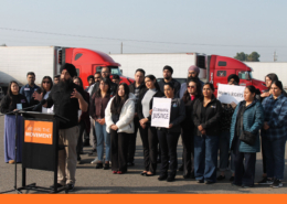 Community advocate speaks at a podium during a Fresno press conference calling for accountability after California DMV commercial license revocations.