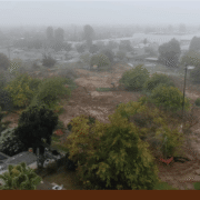 Aerial view of Calwa Park during renovation, showing a foggy construction site with earthwork underway and trees and nearby homes surrounding the area.