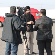 Community advocate speaks to media during a press conference supporting commercial drivers affected by California DMV license revocations, with trucks parked in the background.
