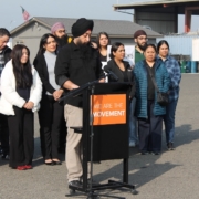 Speaker stands at a podium reading prepared remarks during a Fresno press conference addressing worker rights and commercial driver license revocations.