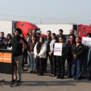 Community advocate speaks at a press conference as supporters hold signs reading “Economic Justice” and “Workers’ Rights” behind him.