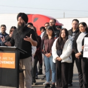 Supporters stand behind a speaker holding an “Economic Justice” sign at a press conference focused on protecting worker rights and livelihoods.