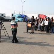 Wide shot of media and community members gathered at a trucking site in Fresno during a press conference addressing California DMV actions affecting drivers.