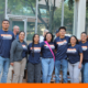 group of six smiling individuals standing outdoors in front of a glass-fronted building. They are wearing matching navy blue t-shirts that read "Better Roads. Safe Streets. Moving Forward Together." They are standing in front of a stack of several cardboard Banker boxes.