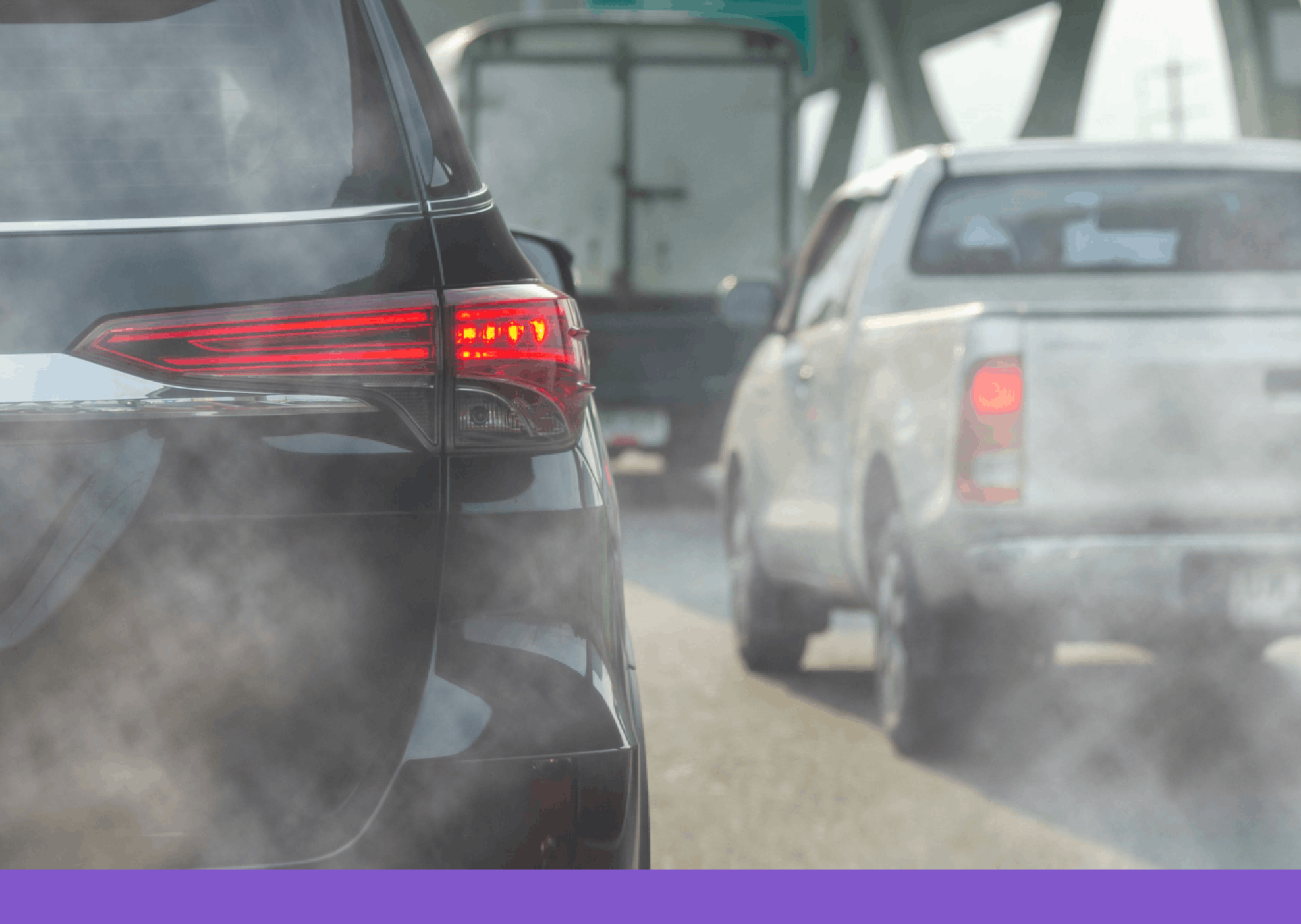 A close-up, eye-level shot from behind a black SUV in heavy traffic on a bright day. Thick, greyish-white exhaust smoke billows from the bottom of the vehicle, partially obscuring the view of a white pickup truck and a larger box truck ahead. The scene captures the visual reality of tailpipe emissions in a congested urban or highway setting, with an overhead green highway sign visible in the blurred background.