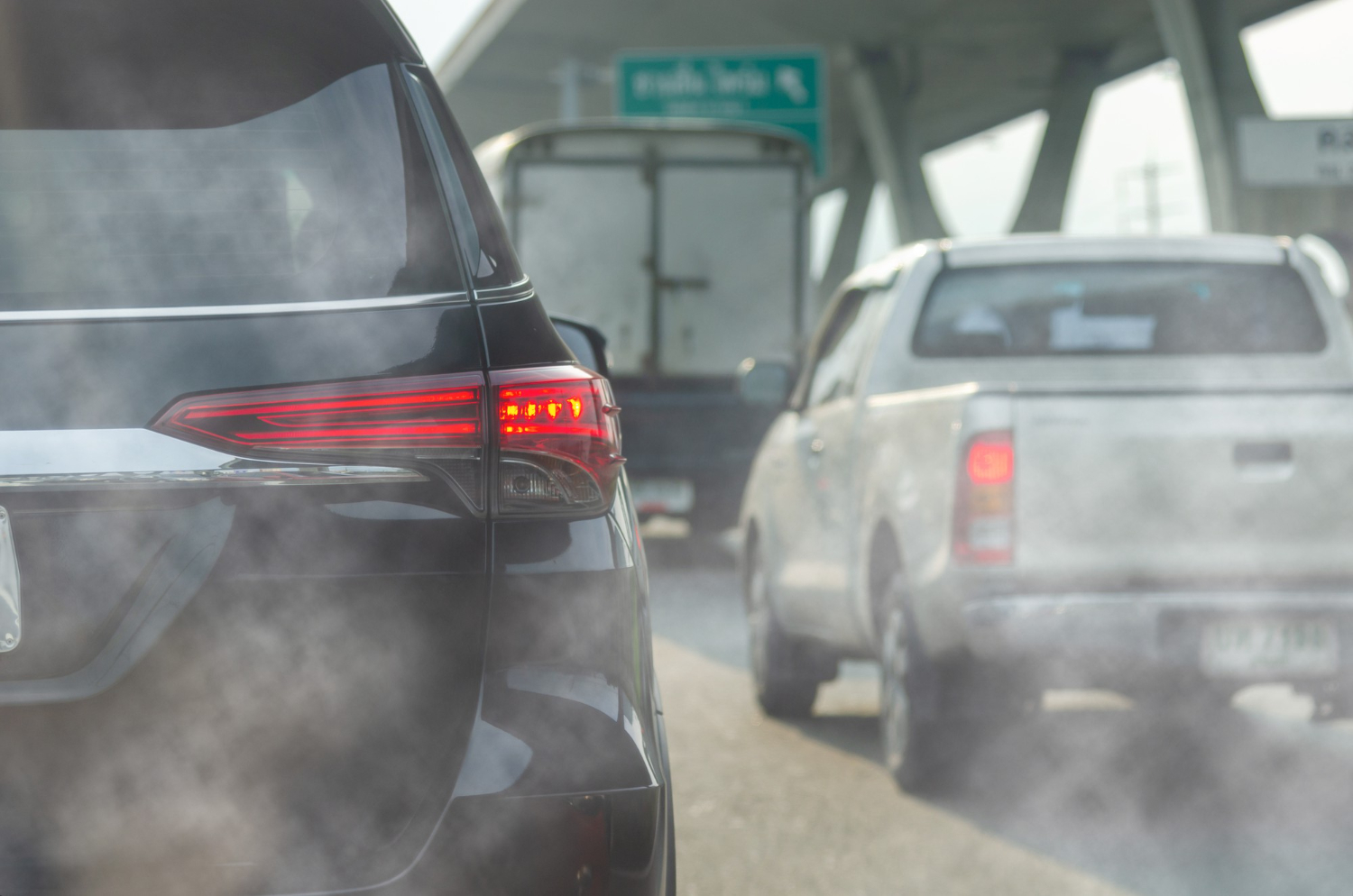A black SUV releasing exhaust emissions while sitting in heavy traffic.