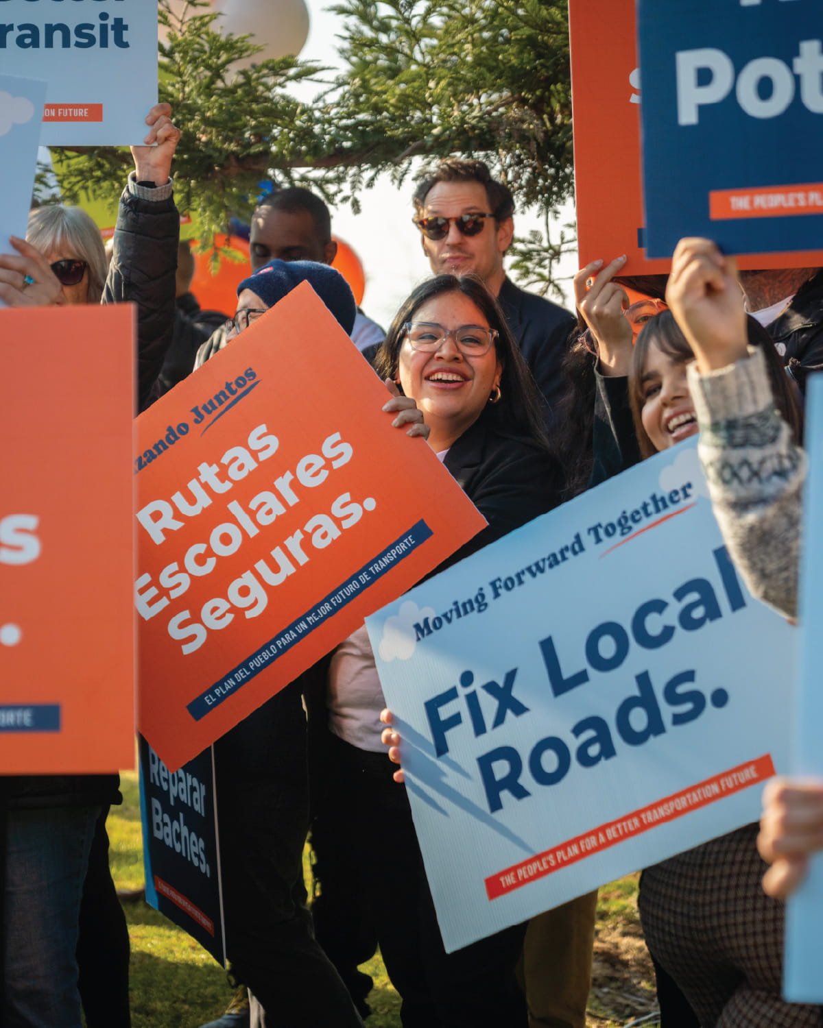 Community members hold signs advocating transportation improvements and safer school routes during an outdoor rally.